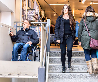 [Translate to Französisch:] Rollstuhlfahrer im Treppenlift eines Einkaufszentrums